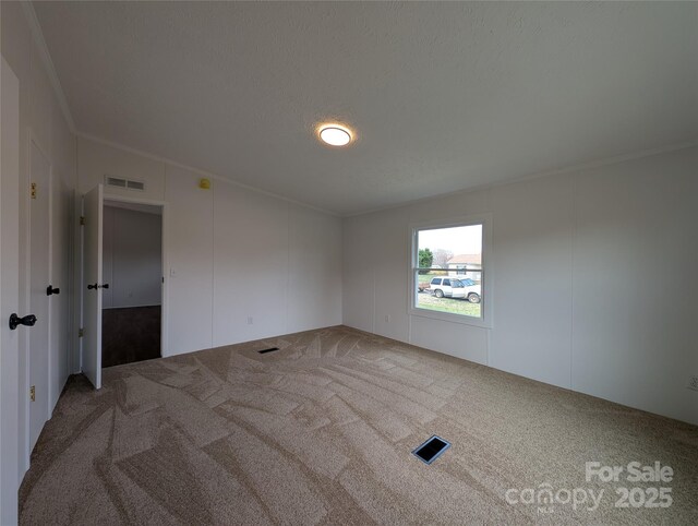 carpeted empty room featuring a textured ceiling, ornamental molding, and visible vents