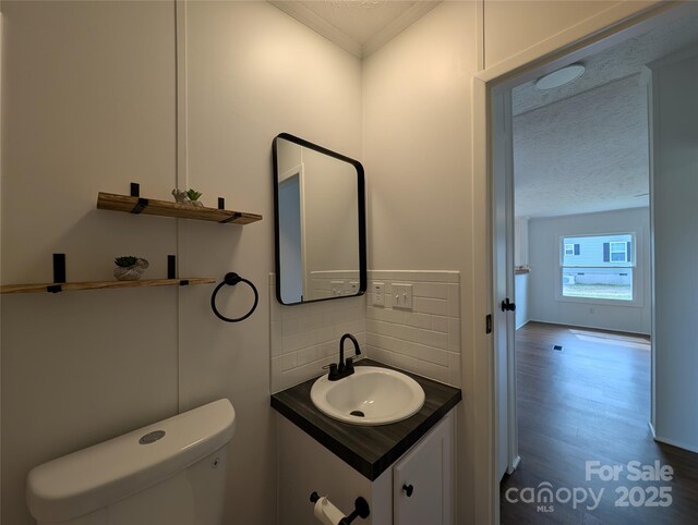half bathroom with a textured ceiling, ornamental molding, toilet, vanity, and backsplash