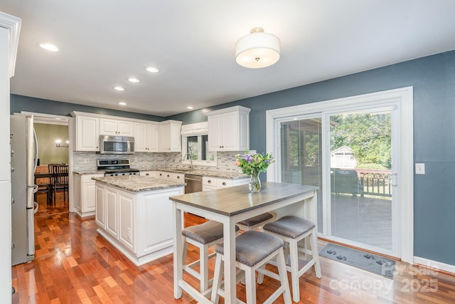 kitchen with light wood finished floors, a sink, stainless steel appliances, tasteful backsplash, and a center island