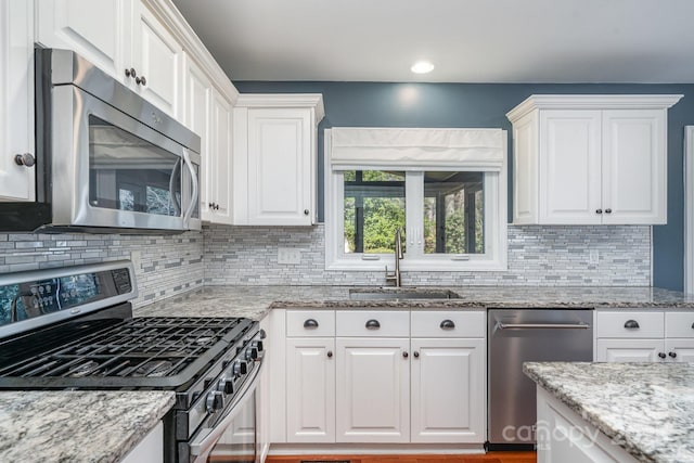 kitchen featuring white cabinets, light stone countertops, stainless steel appliances, and a sink