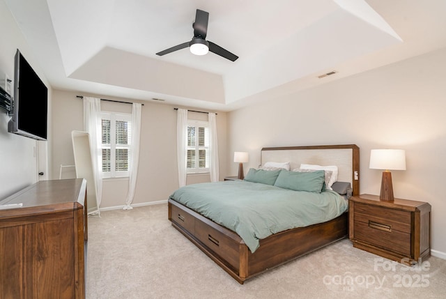 bedroom featuring a tray ceiling, baseboards, light colored carpet, and visible vents