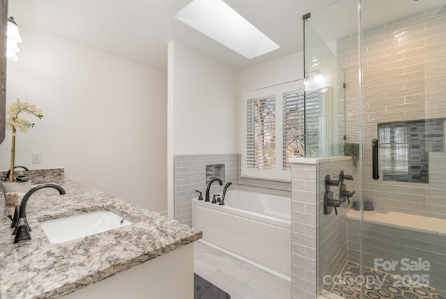 full bathroom featuring tile patterned floors, a stall shower, a skylight, a bath, and a sink