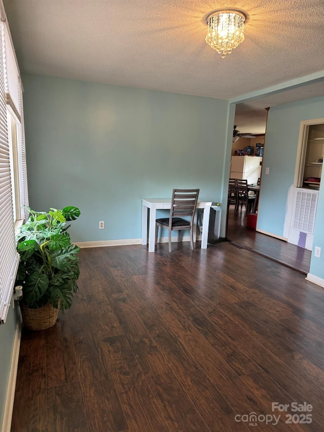 spare room featuring visible vents, baseboards, wood finished floors, a notable chandelier, and a textured ceiling