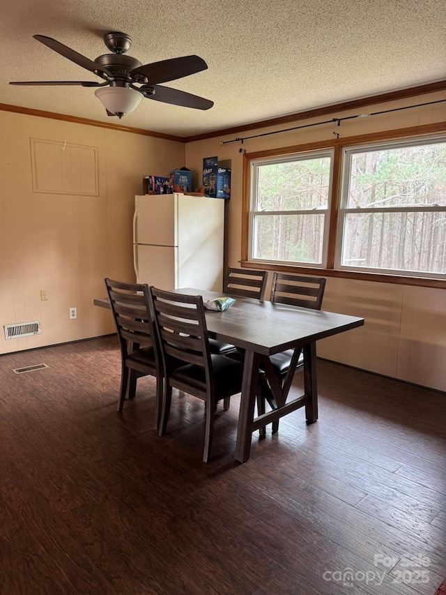 dining space featuring dark wood-style floors, visible vents, a textured ceiling, and ornamental molding