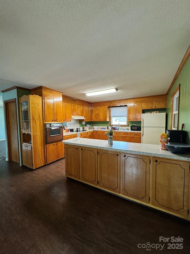 kitchen with ornamental molding, dark wood-style floors, freestanding refrigerator, wall oven, and light countertops