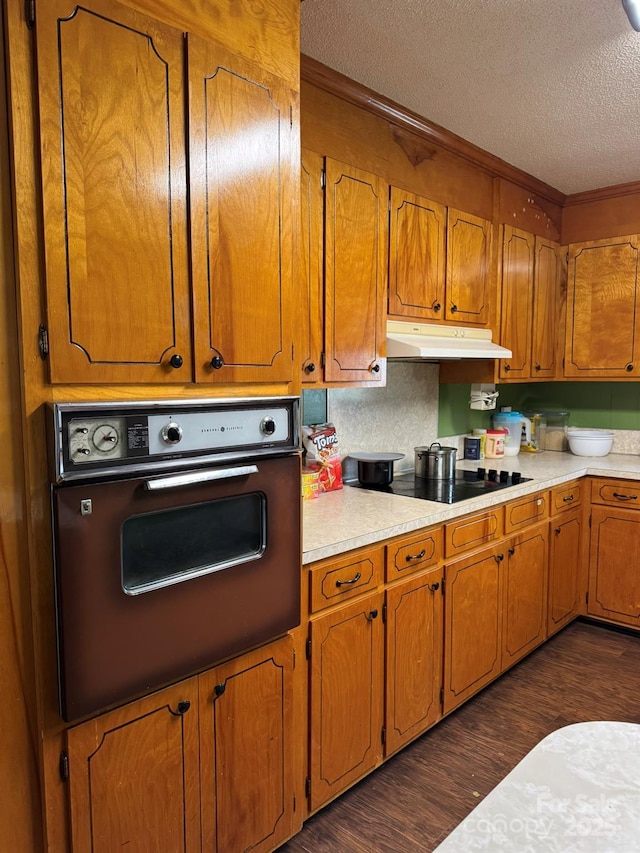 kitchen featuring under cabinet range hood, a textured ceiling, dark wood-style floors, wall oven, and black electric cooktop