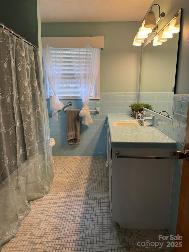 bathroom with tile patterned flooring, vanity, wainscoting, a shower with curtain, and tile walls