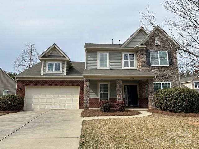 craftsman-style house featuring a garage, stone siding, brick siding, and driveway