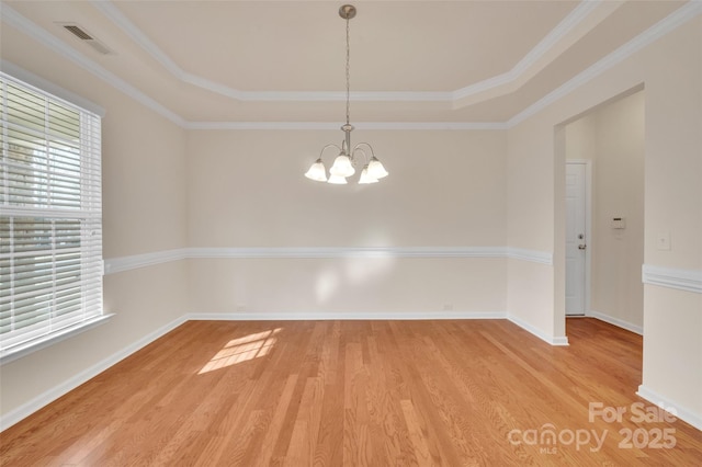 empty room with a raised ceiling, ornamental molding, an inviting chandelier, light wood finished floors, and baseboards