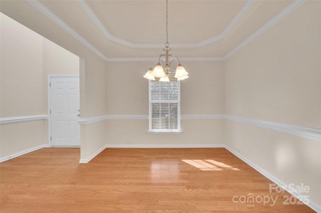 spare room featuring a raised ceiling, an inviting chandelier, baseboards, and light wood finished floors