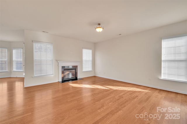 unfurnished living room with a glass covered fireplace, light wood-style flooring, baseboards, and a healthy amount of sunlight