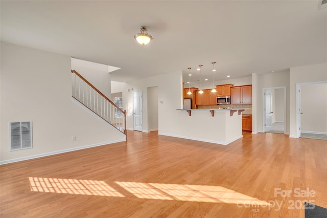 unfurnished living room with visible vents, light wood-type flooring, and baseboards