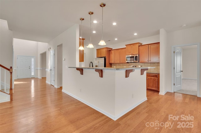 kitchen with a breakfast bar, light wood-style floors, backsplash, and stainless steel appliances