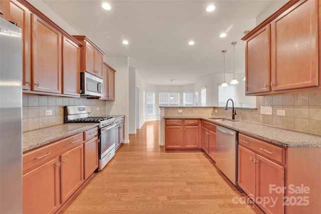 kitchen featuring a sink, light stone counters, stainless steel appliances, a peninsula, and light wood finished floors