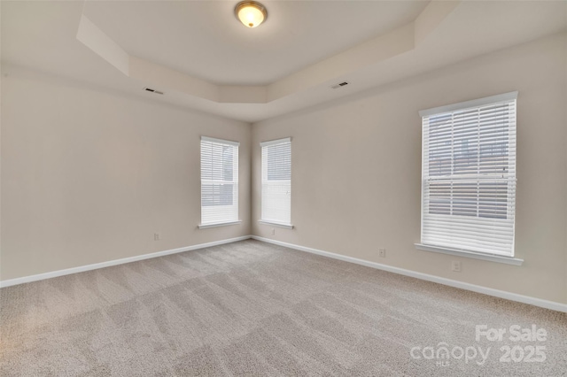 carpeted empty room with a raised ceiling, visible vents, and baseboards