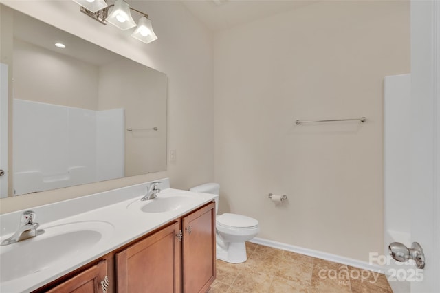 bathroom with double vanity, toilet, baseboards, and a sink