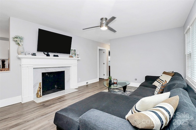 living room with a premium fireplace, baseboards, wood finished floors, and a ceiling fan