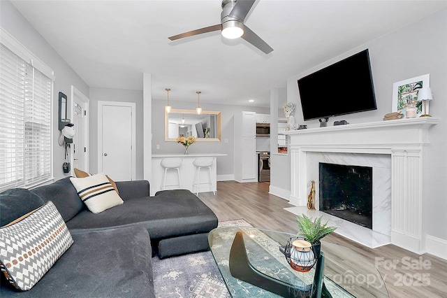 living area featuring ceiling fan, baseboards, wood finished floors, and a fireplace