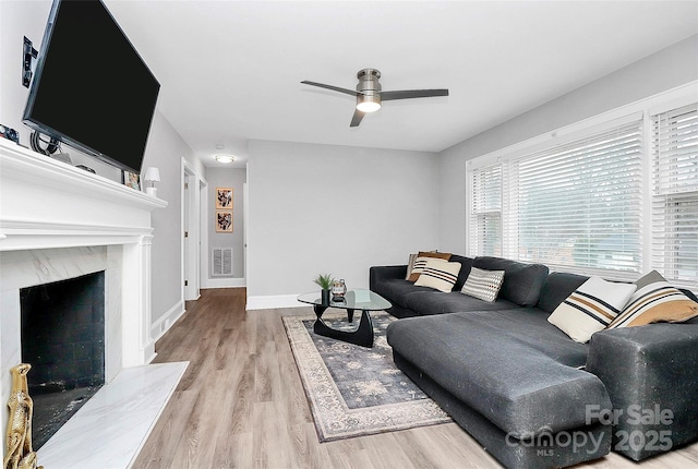 living room featuring visible vents, ceiling fan, baseboards, a fireplace, and wood finished floors