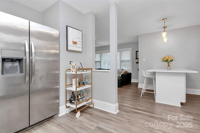 kitchen with baseboards, a breakfast bar, light countertops, light wood-style floors, and stainless steel fridge