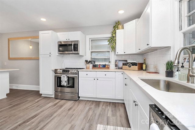 kitchen with light wood-type flooring, a sink, stainless steel appliances, white cabinetry, and tasteful backsplash