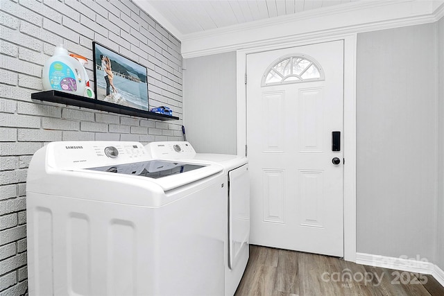 washroom featuring light wood-style flooring, ornamental molding, washer and dryer, brick wall, and laundry area