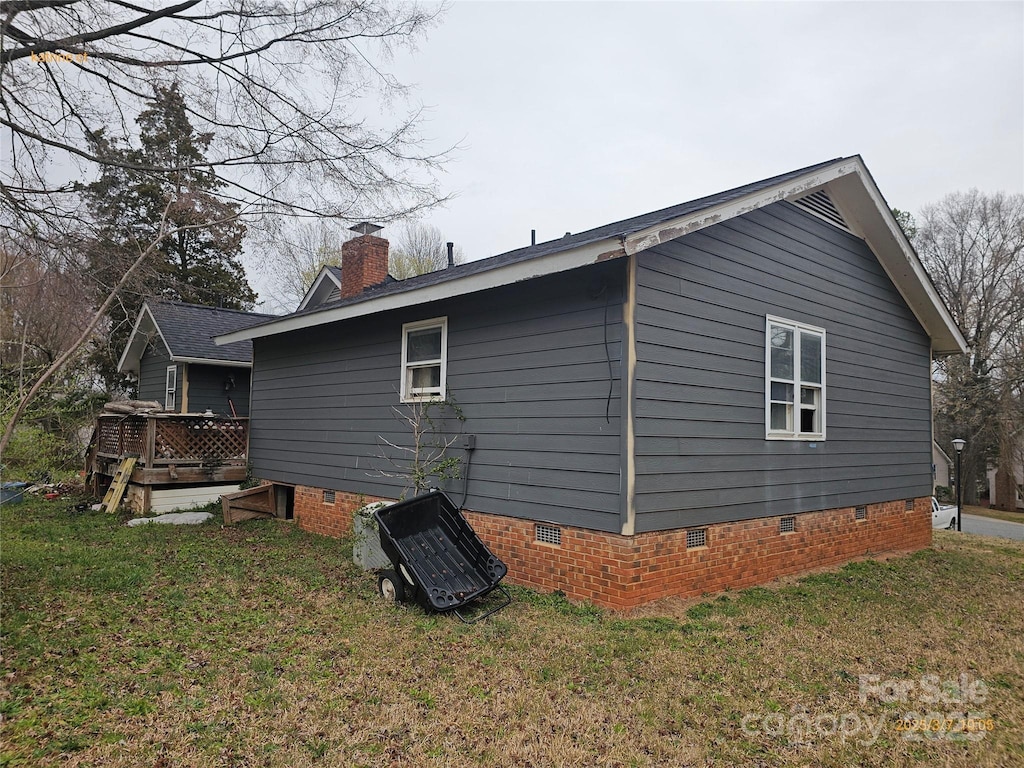 view of side of home with crawl space, a yard, a deck, and a chimney