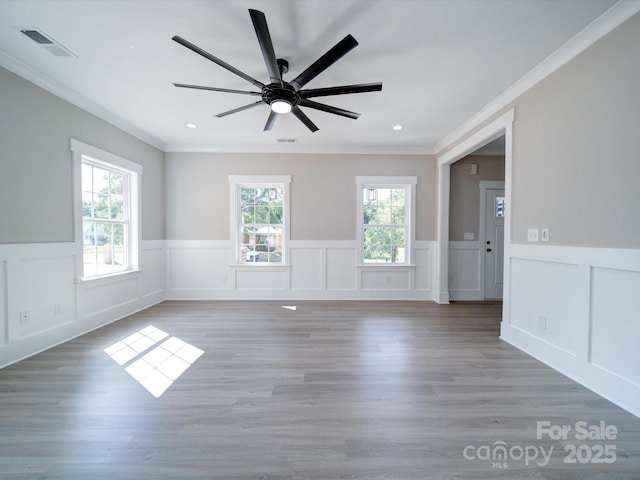 empty room with a wealth of natural light, visible vents, light wood-type flooring, and ornamental molding