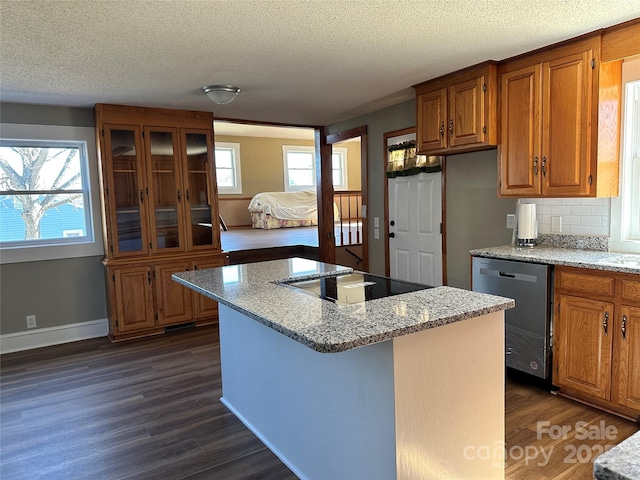 kitchen with brown cabinetry, dark wood finished floors, stainless steel dishwasher, black electric cooktop, and a center island