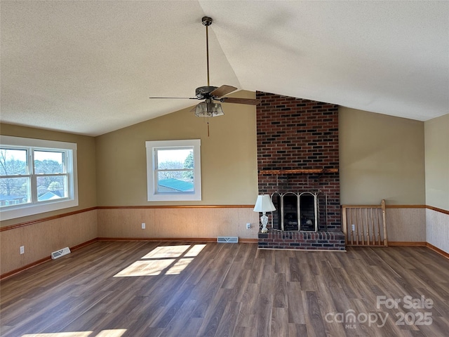 unfurnished living room featuring a textured ceiling, lofted ceiling, plenty of natural light, and wainscoting