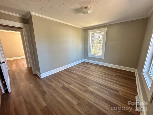 spare room featuring dark wood-type flooring, baseboards, visible vents, and ornamental molding