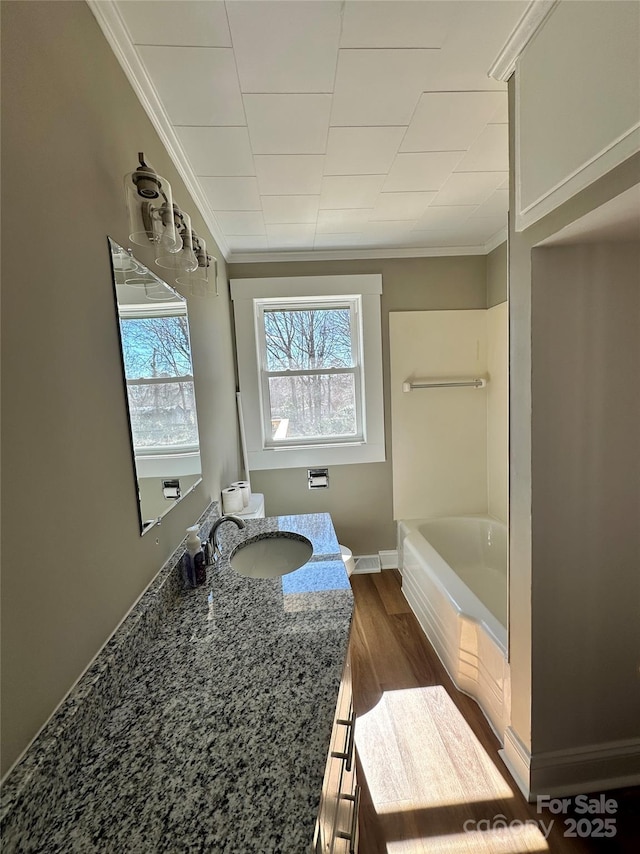 full bathroom featuring crown molding, baseboards, a bathing tub, wood finished floors, and vanity