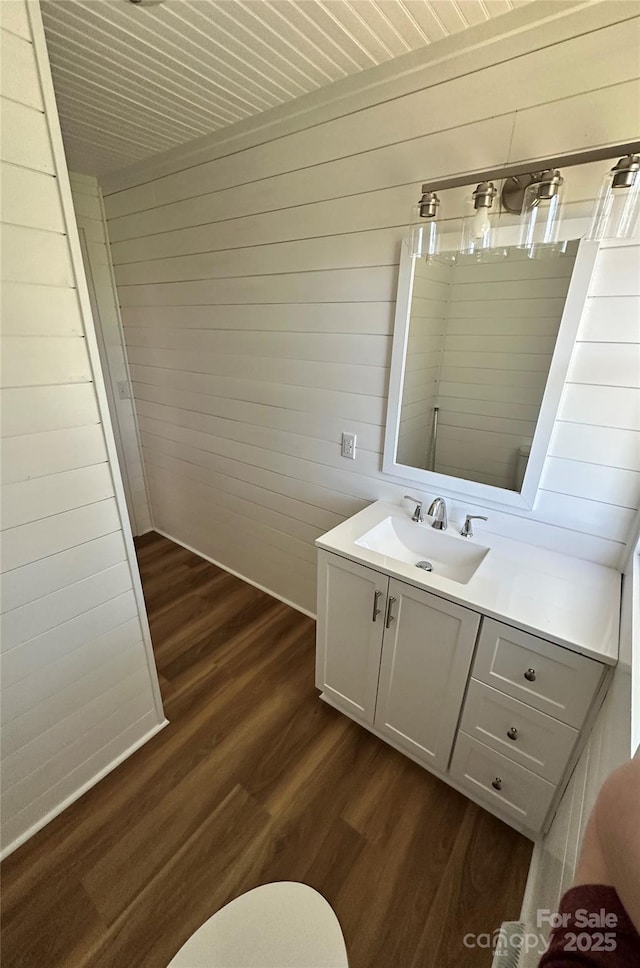 bathroom featuring wooden walls, toilet, vanity, and wood finished floors