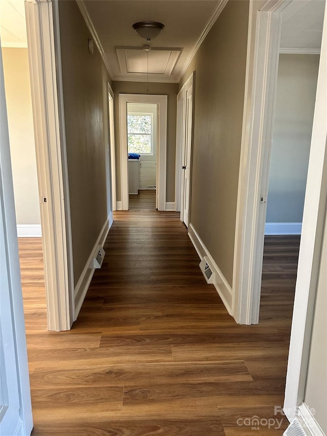 hallway with wood finished floors, visible vents, baseboards, attic access, and ornamental molding