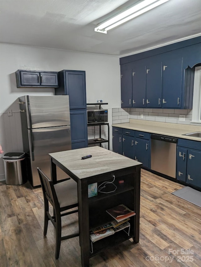 kitchen with appliances with stainless steel finishes, light countertops, blue cabinets, and wood finished floors