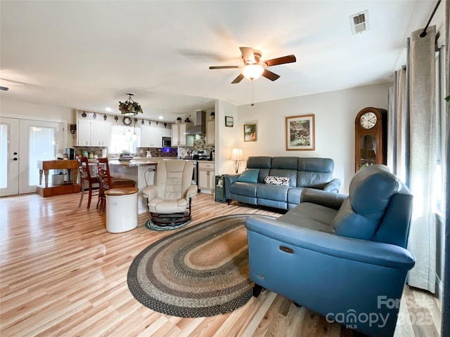 living area featuring visible vents, light wood-style floors, a ceiling fan, and french doors