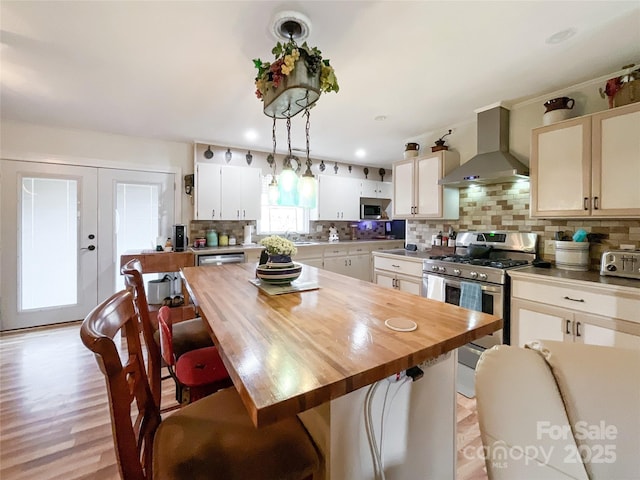 kitchen with butcher block countertops, decorative backsplash, appliances with stainless steel finishes, and wall chimney range hood