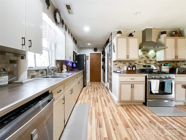 kitchen with visible vents, wall chimney range hood, light wood-style floors, stainless steel appliances, and a sink