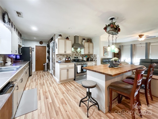 kitchen featuring visible vents, stainless steel appliances, wood counters, a kitchen breakfast bar, and wall chimney exhaust hood