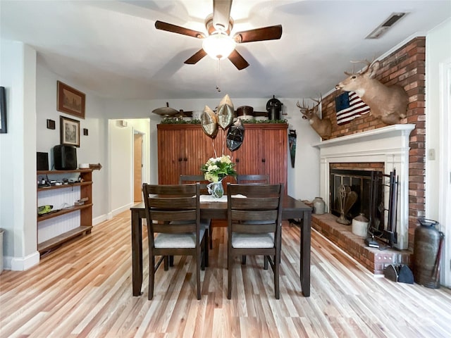 dining room with visible vents, a ceiling fan, light wood-style floors, a fireplace, and baseboards