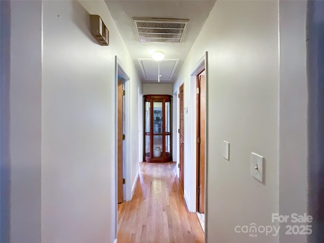 hallway featuring light wood-type flooring, visible vents, and attic access