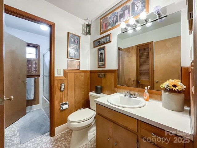 full bath with vanity, a wainscoted wall, wood walls, toilet, and combined bath / shower with glass door