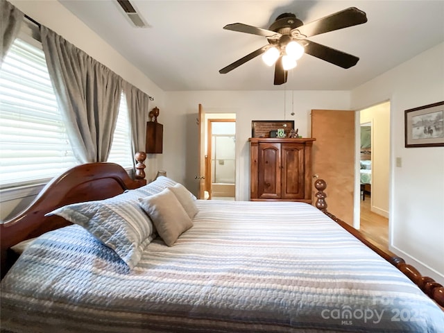 bedroom with a ceiling fan, visible vents, wood finished floors, baseboards, and ensuite bathroom