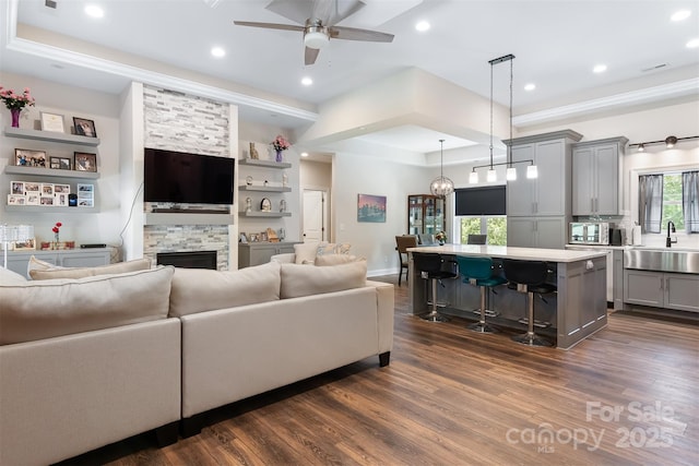 living room featuring a raised ceiling, recessed lighting, a fireplace, and dark wood-style flooring