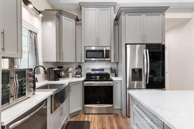 kitchen featuring light wood finished floors, gray cabinetry, light stone countertops, decorative backsplash, and appliances with stainless steel finishes