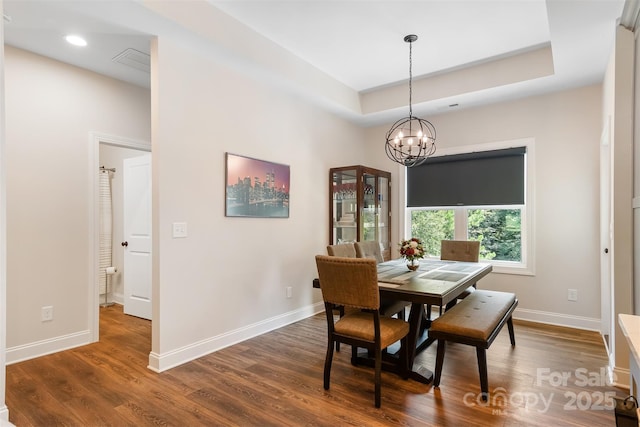 dining space with a tray ceiling, an inviting chandelier, dark wood-type flooring, and baseboards