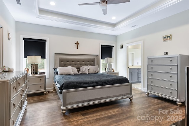 bedroom with dark wood finished floors, a tray ceiling, recessed lighting, and ensuite bath