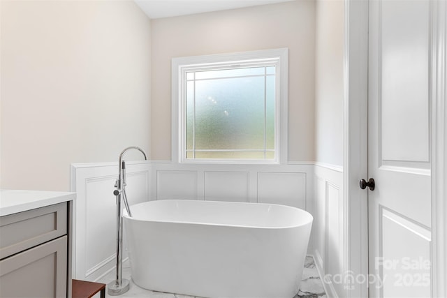 bathroom featuring a wainscoted wall, vanity, a decorative wall, and a freestanding tub