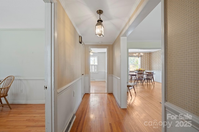 corridor featuring wallpapered walls, a notable chandelier, a wainscoted wall, and light wood finished floors