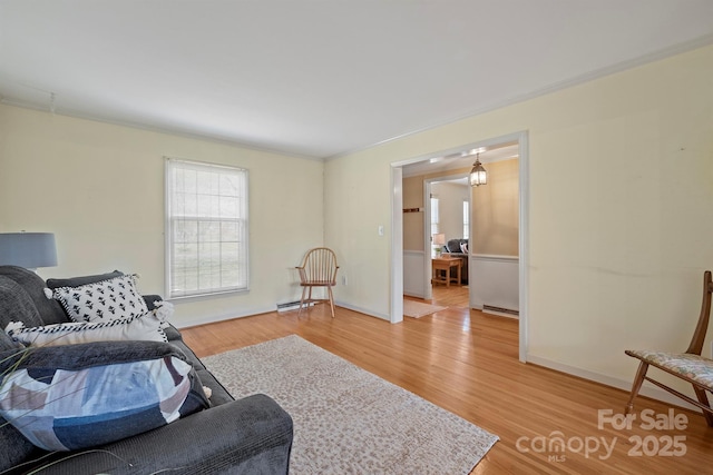 living room with a baseboard heating unit, baseboards, wood finished floors, and ornamental molding